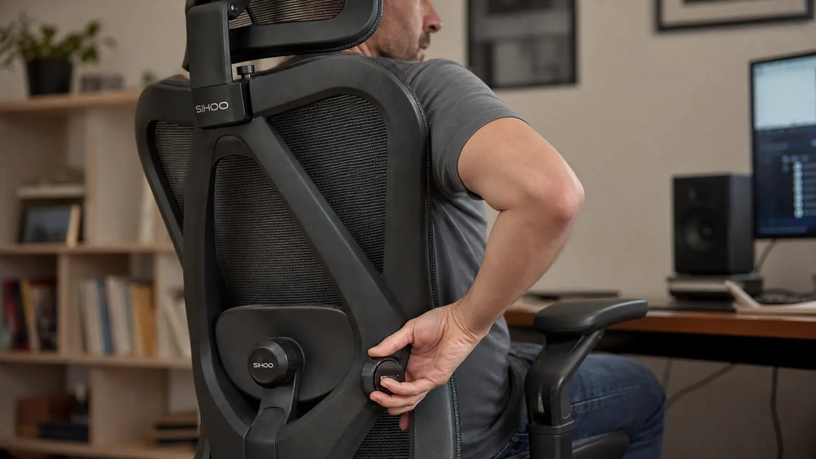 Close-up of a hand adjusting the lumbar support dial on the back of a mesh office chair