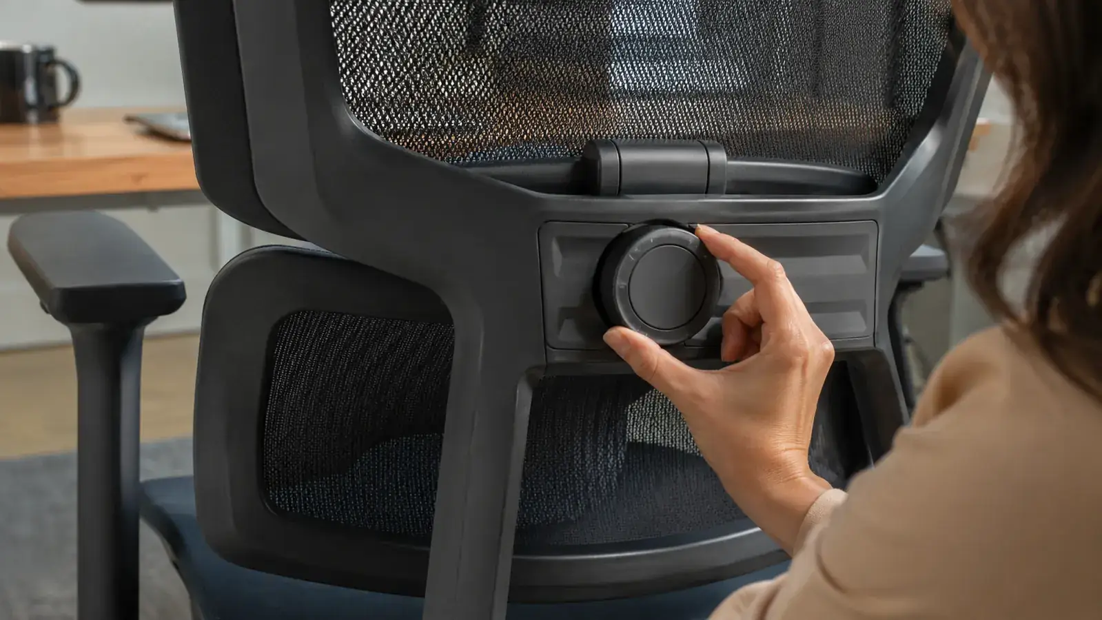 Close-up of a hand adjusting the lumbar support dial on the back of a mesh office chair
