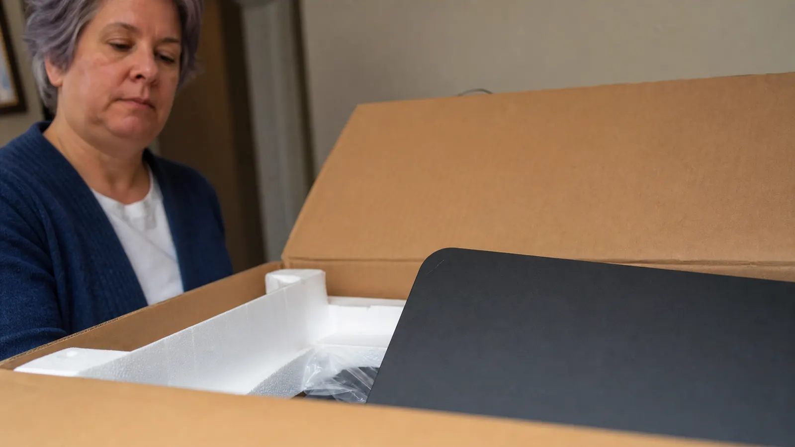 Opened cardboard shipping box with foam packing material and a black desk converter panel showing a visible scratch near the corner